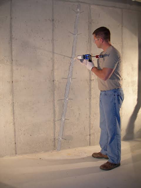Technician injecting polyurethane foam sealer into a concrete foundation wall crack.